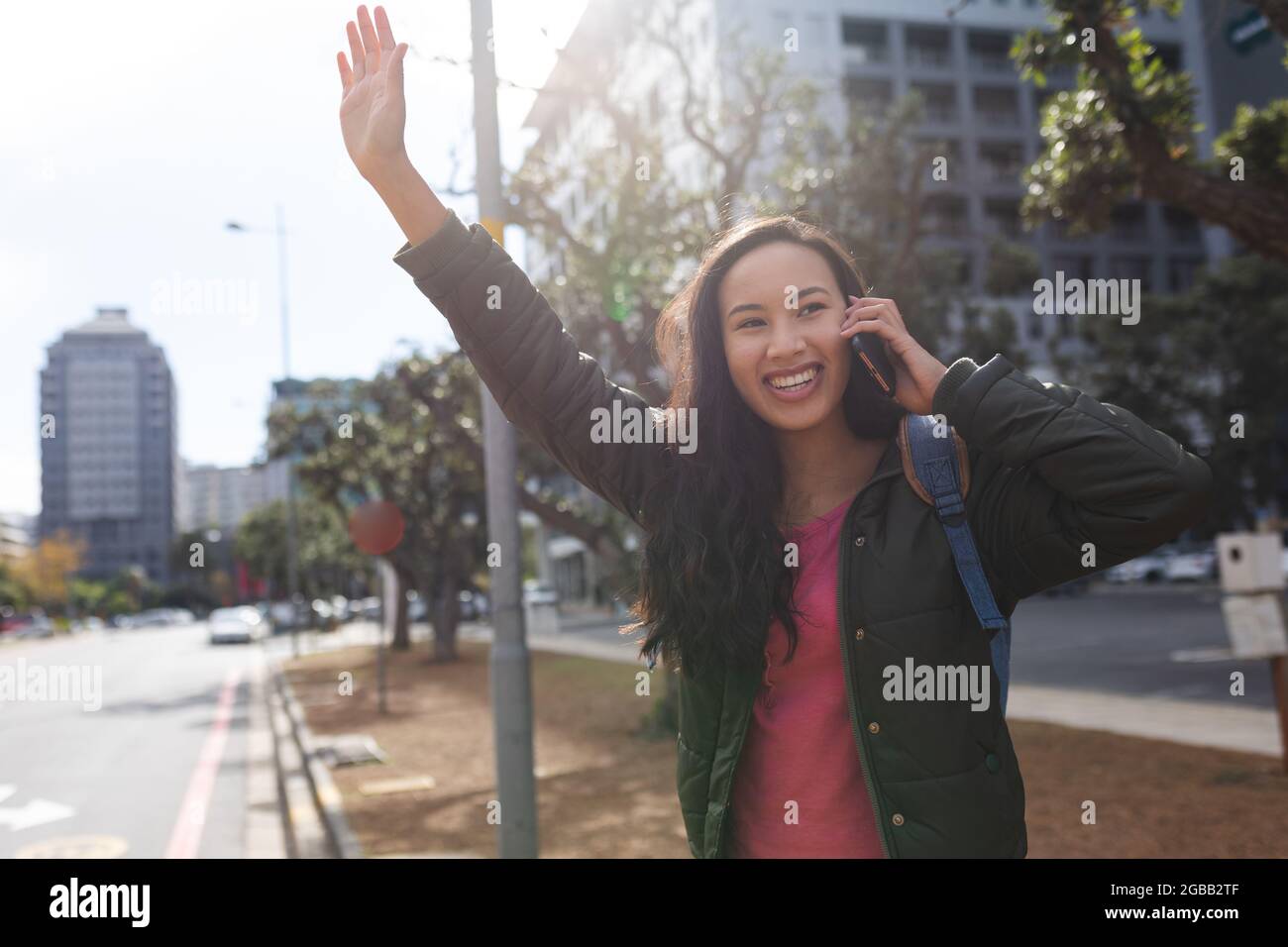 Femme asiatique debout sur la route qui hante un taxi, parlant sur un smartphone Banque D'Images