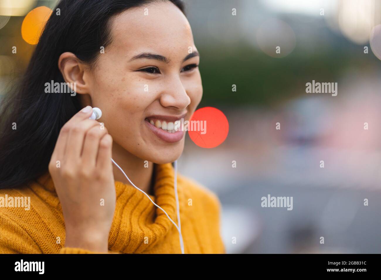 Femme asiatique souriante portant des écouteurs dans la rue Banque D'Images