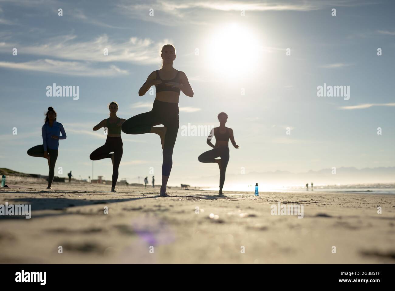 Groupe d'amis féminins divers pratiquant le yoga à la plage Banque D'Images