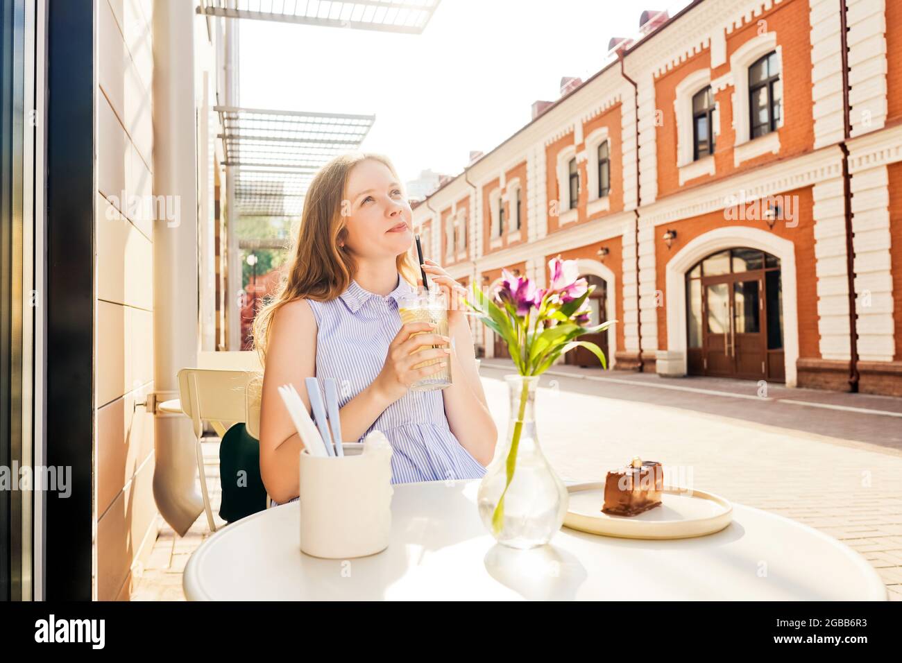 Une jeune femme boit de la limonade dans un café d'été. Rue en arrière-plan. Banque D'Images