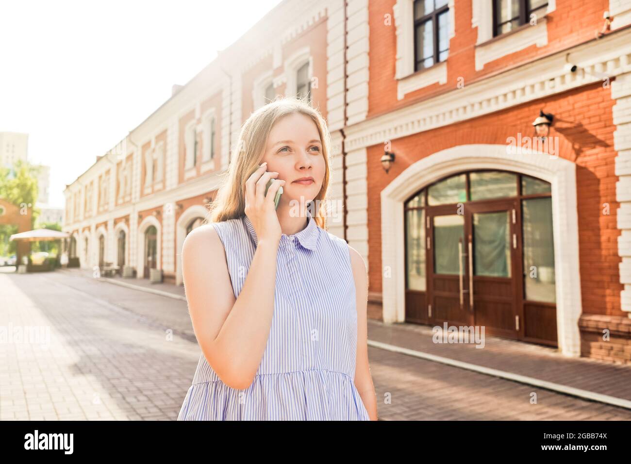 Gros plan d'une belle jeune femme souriante parlant sur un téléphone mobile à l'extérieur. Rue en arrière-plan, jour d'été. Banque D'Images