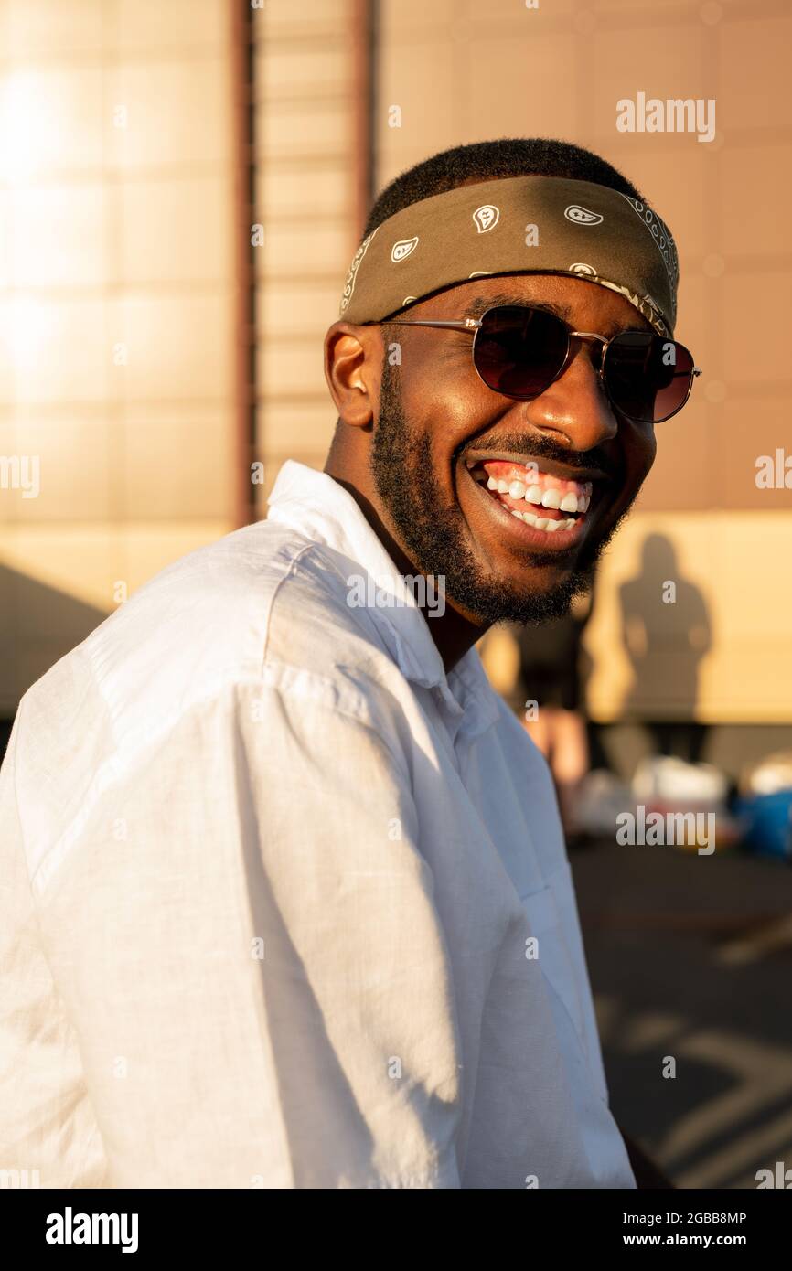 Homme africain joyeux en chemise blanche, lunettes de soleil et serre-tête  appréciant la fête en plein air Photo Stock - Alamy