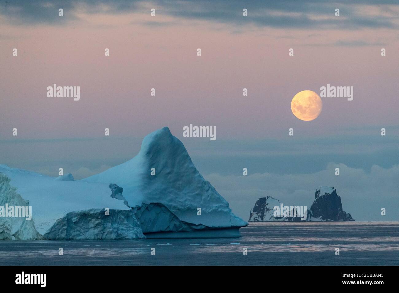 Presque pleine lune au-dessus de petites îles et icebergs au large de la péninsule Trinity, Antarctique, régions polaires Banque D'Images