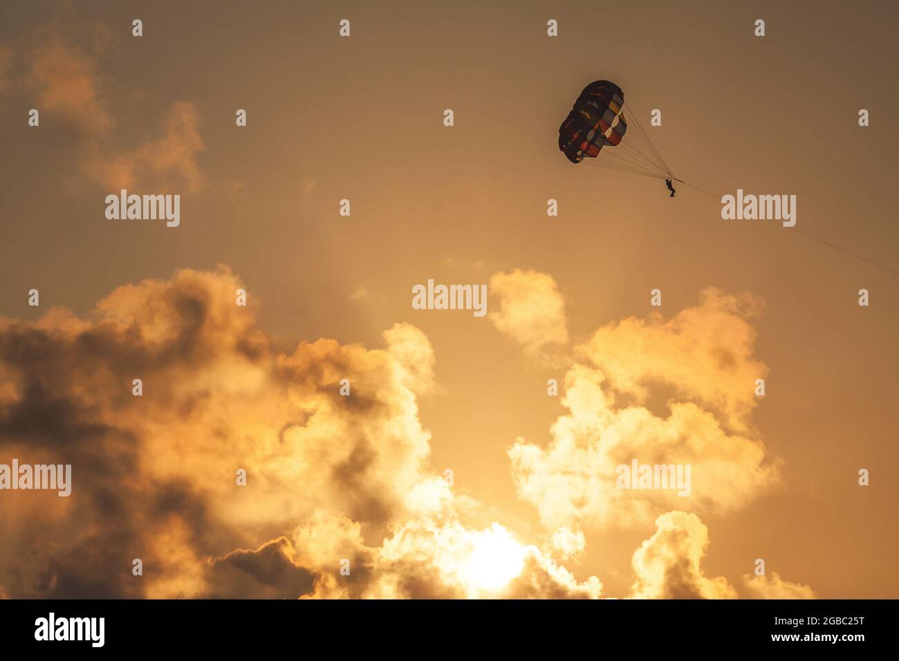 Parachute ascensionnel au coucher du soleil. Silhouette d'une personne avec parachute contre le ciel orange du soir avec nuages. Banque D'Images