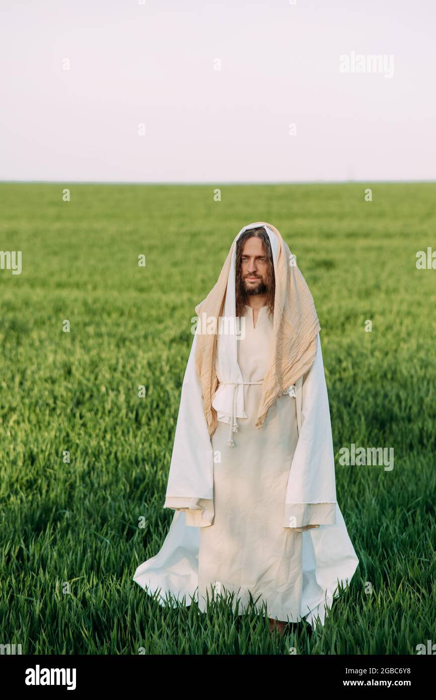 Jésus Christ debout dans la prairie vêtu de sa robe blanche traditionnelle sur fond de ciel. Banque D'Images