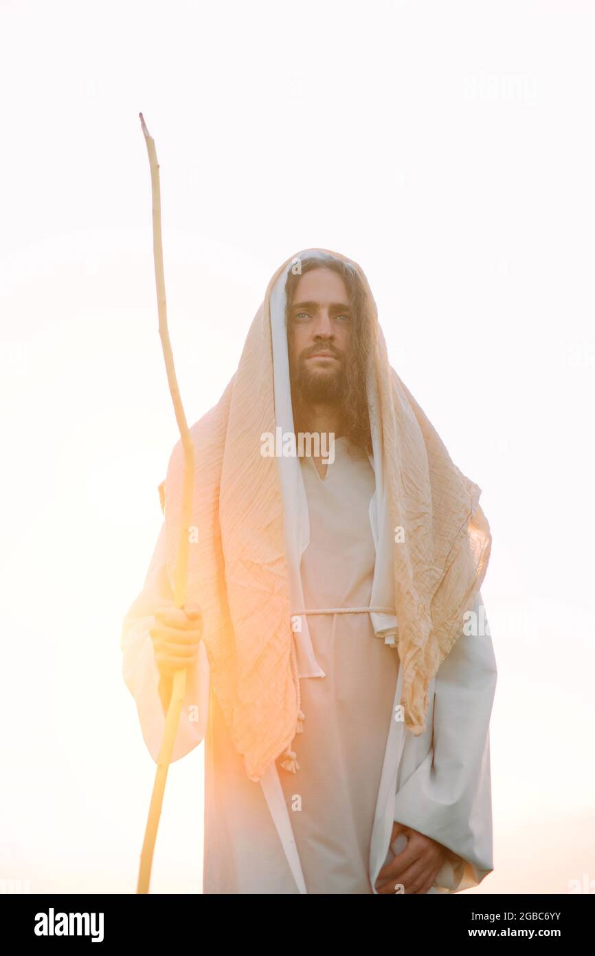 Jésus Christ avec son personnel en bois se tient dans sa robe blanche  traditionnelle contre le ciel et le coucher du soleil Photo Stock - Alamy