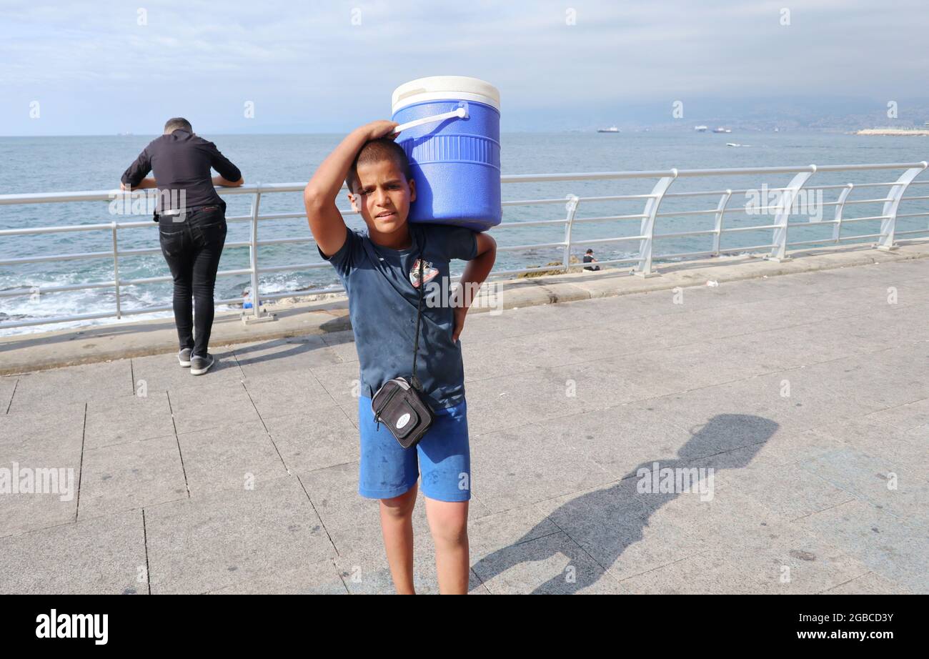 Un enfant syrien vend de l'eau sur la promenade du bord de mer de Corniche, à Beyrouth, au Liban, le 20 2021 juillet. Selon le dernier rapport Save the Children on Lebanon, « des centaines de milliers d’enfants au Liban vont se coucher sous la faim, car leurs parents ne parviennent pas de plus en plus à joindre les deux bouts à la fin de chaque mois et sont incapables de payer pour des éléments essentiels comme la nourriture, l’électricité et la médecine. [...] La crise économique a touché des familles de tous les niveaux socio-économiques et de toutes les nationalités, mais les réfugiés syriens sont parmi les plus durement touchés. Neuf familles syriennes sur 10 au Liban vivent dans une pauvreté extrême. Beaucoup sont c Banque D'Images