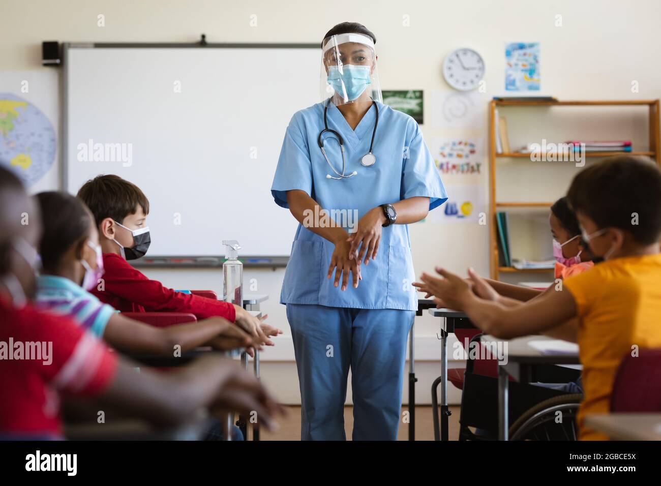 Une travailleuse de la santé montrant aux élèves qu'ils doivent utiliser un désinfectant pour les mains à l'école primaire Banque D'Images