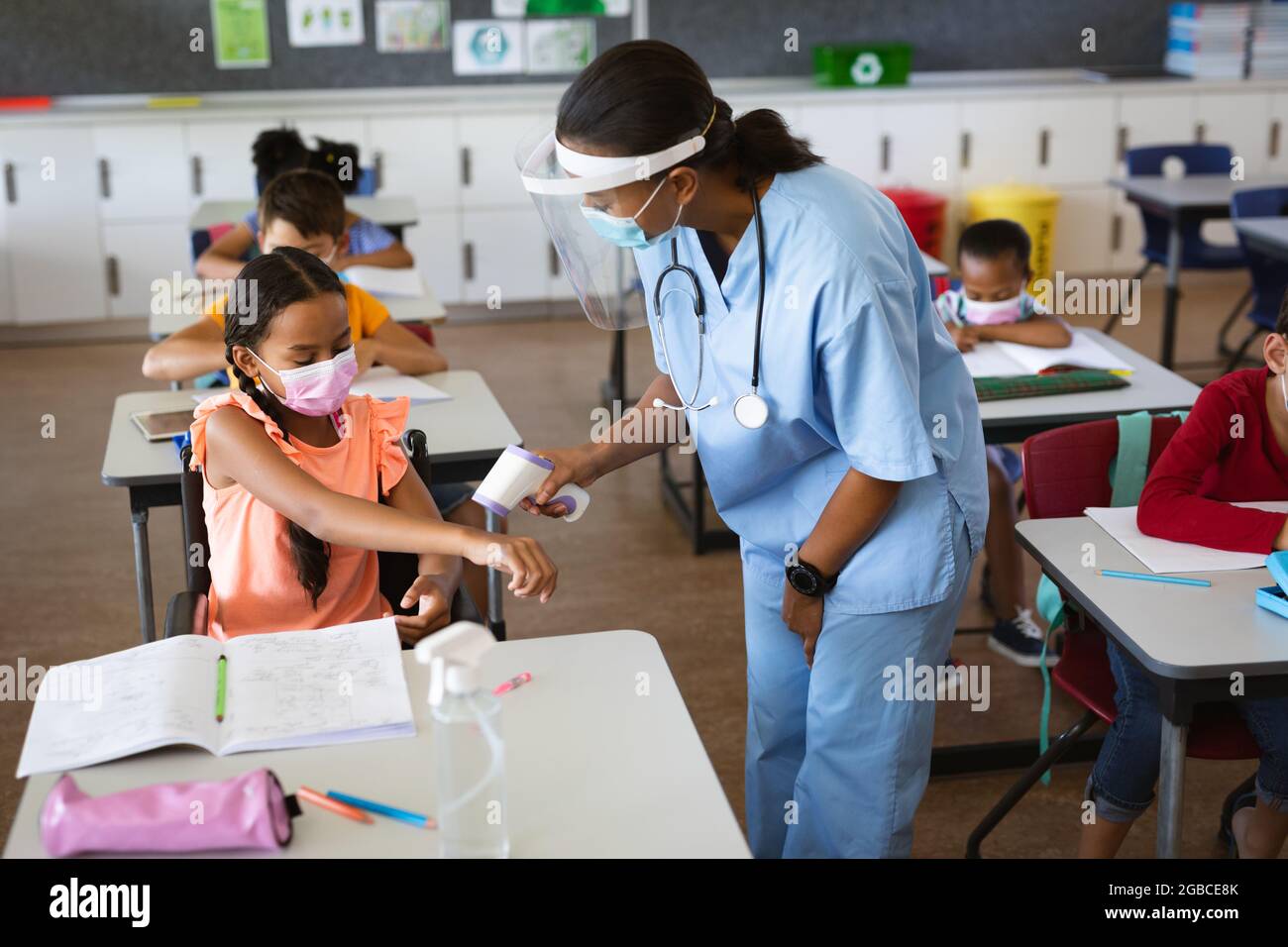 Une travailleuse de santé portant un écran facial mesurant la température d'une fille handicapée à l'école primaire Banque D'Images