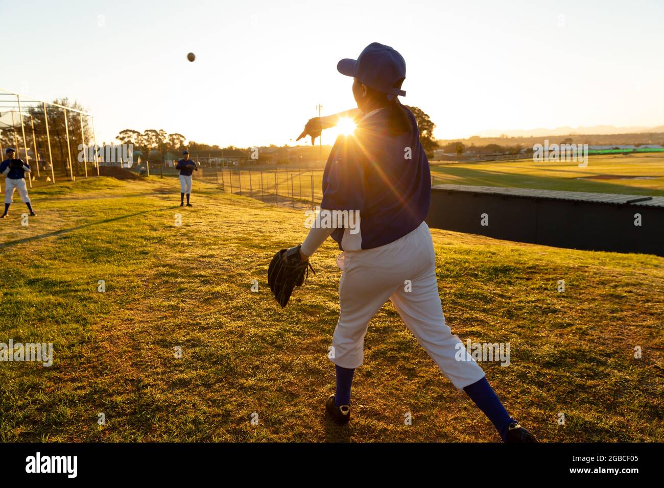 Un groupe diversifié de joueuses de baseball se réchauffent sur le terrain au lever du soleil, lancent et attrapent le ballon Banque D'Images