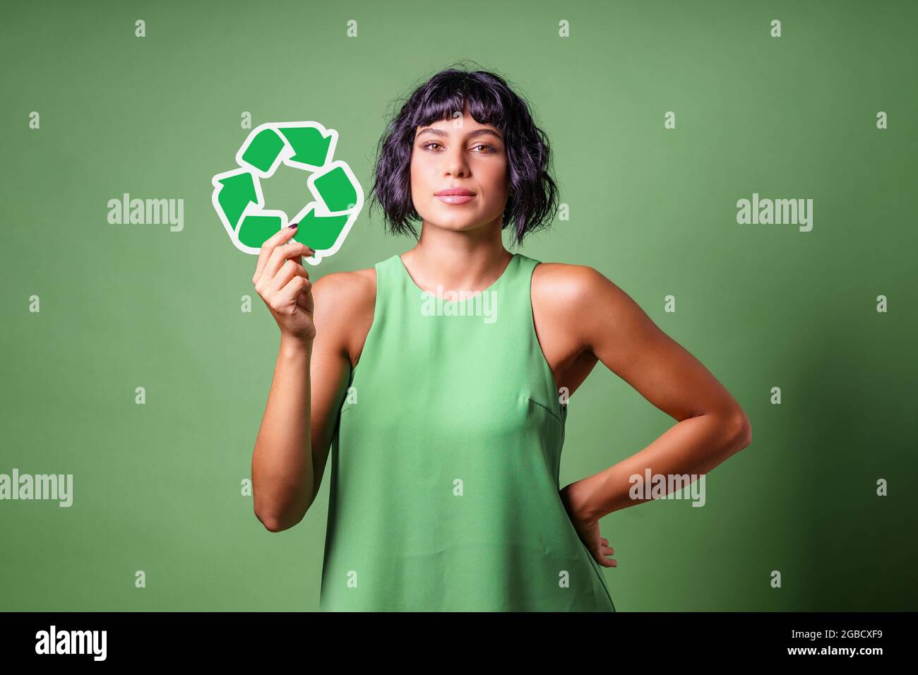 Jeune femme en vert montrant le symbole de recyclage isolé sur un fond vert. Concept de durabilité. Banque D'Images