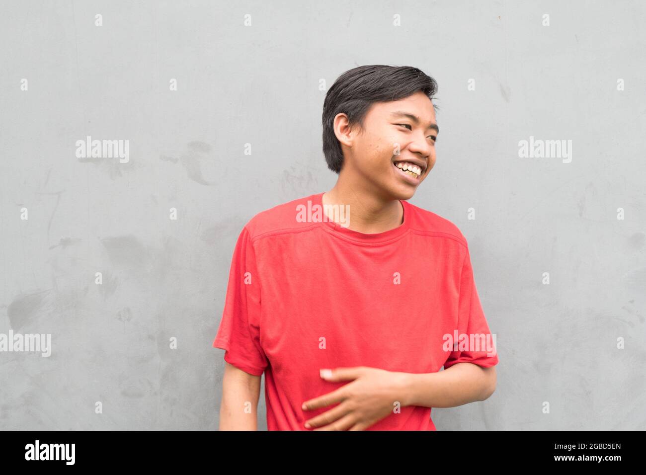 Gros plan d'un jeune homme dans un T-shirt rouge riant. Banque D'Images