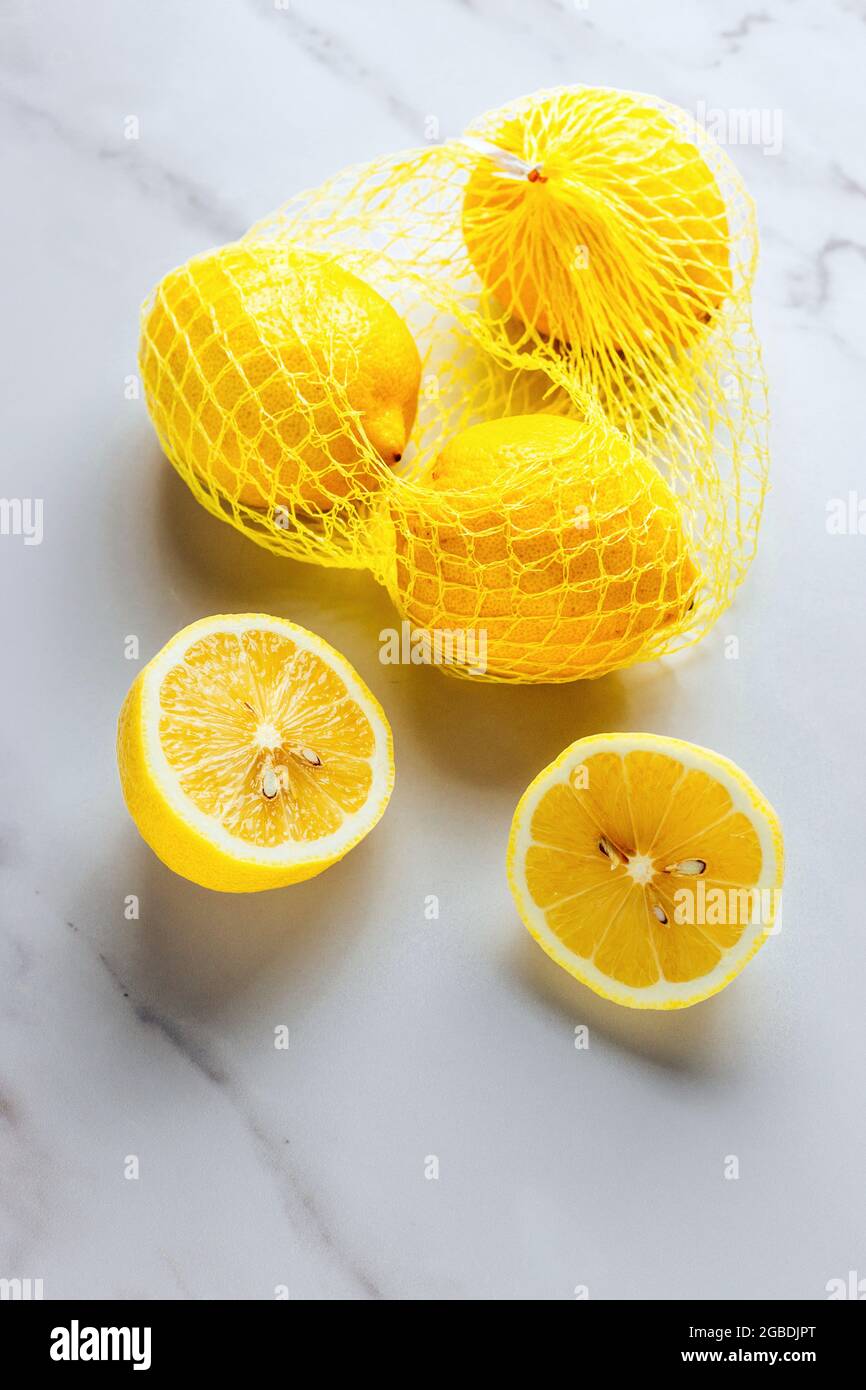 Lemons frais sur fond de marbre blanc avec des citrons entiers, des demi-citrons et des citrons dans le Net Packaging - COPYSPACE POUR LE TEXTE, FOOPPIX BLANC Banque D'Images