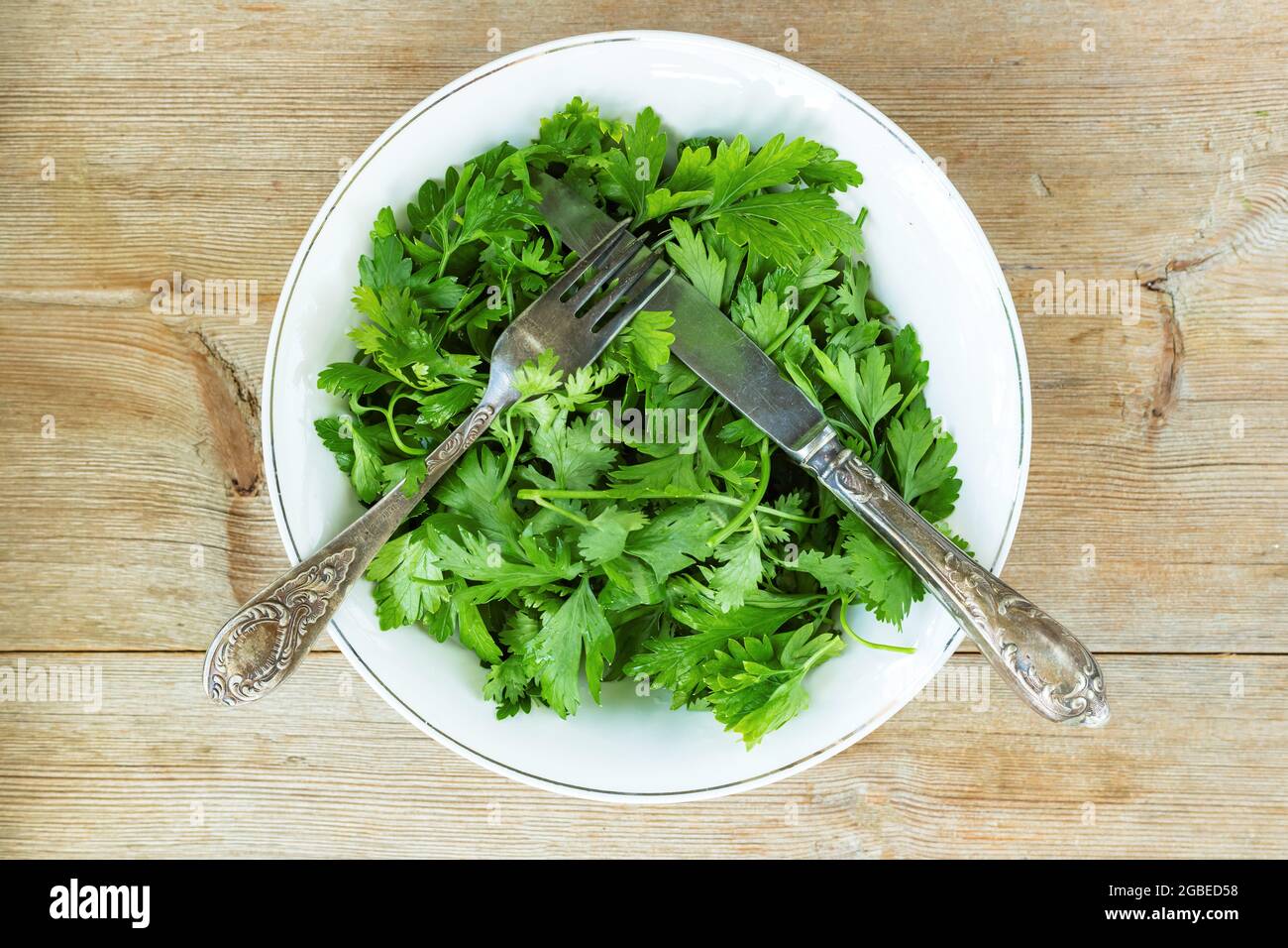 Salade verte d'herbes de coriandre de persil sur l'assiette, fourchette, couteau sur l'ancienne table en bois. Concept de détox Banque D'Images