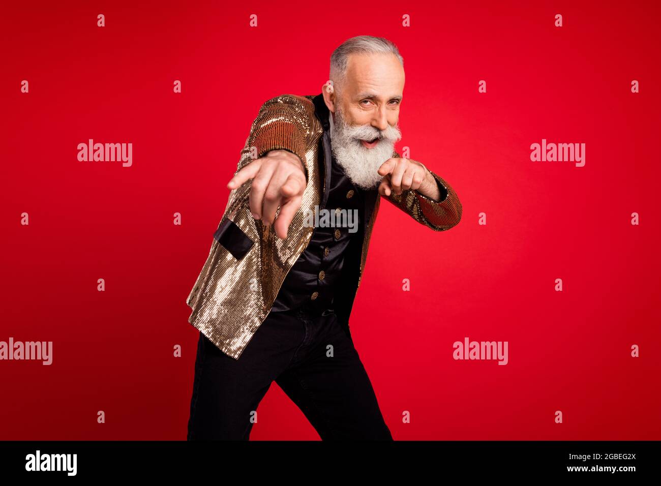 Photo d'une belle barbe grise homme illusionniste d'âge indique que vous portez un costume d'or isolé sur fond rouge Banque D'Images