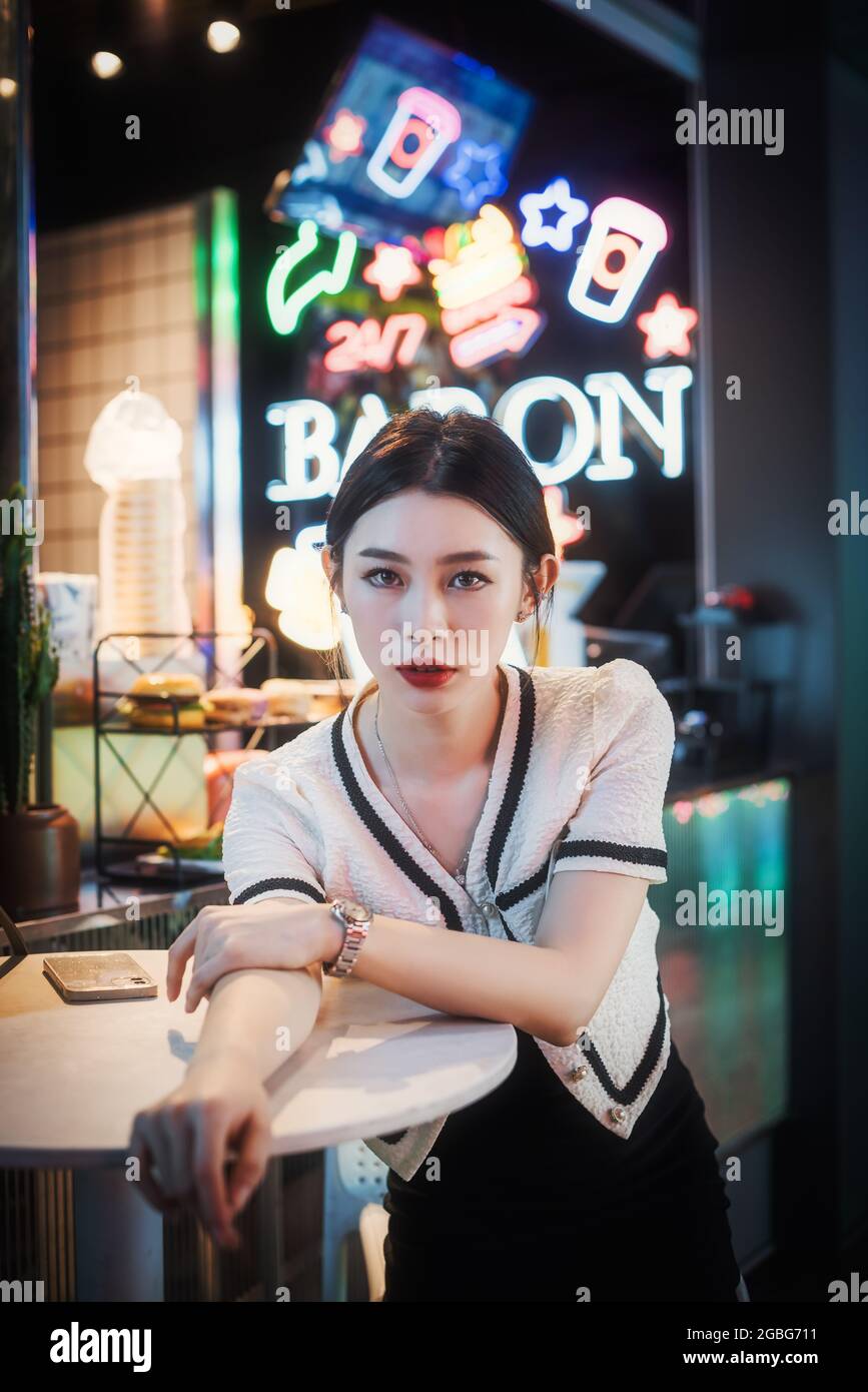 Jeune femme chinoise assise à une table avec des néons en arrière-plan à Chengdu, province du Sichuan, en Chine Banque D'Images