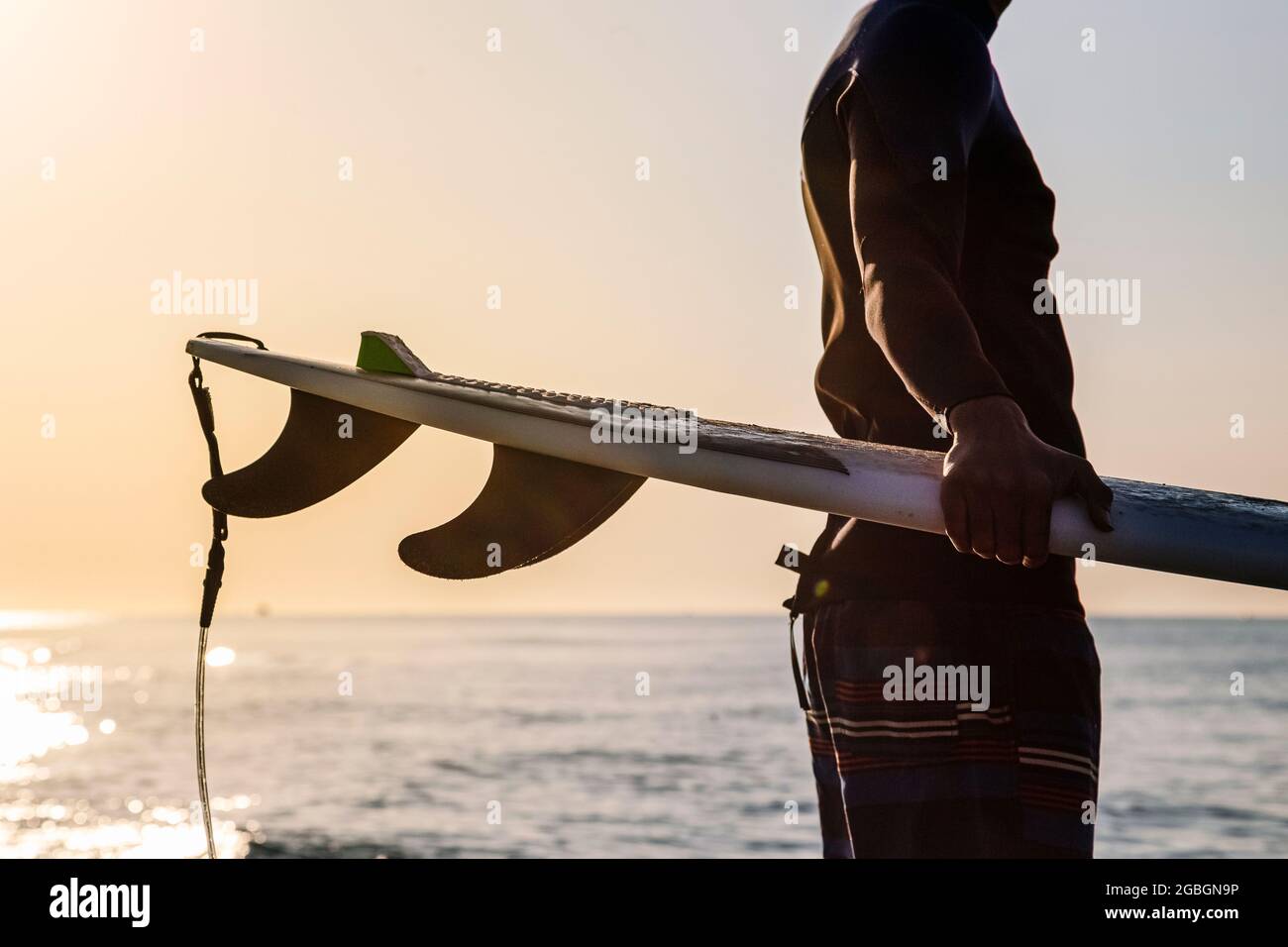 Surfeur méconnaissable se préparant à surfer sur la plage au lever du soleil Banque D'Images