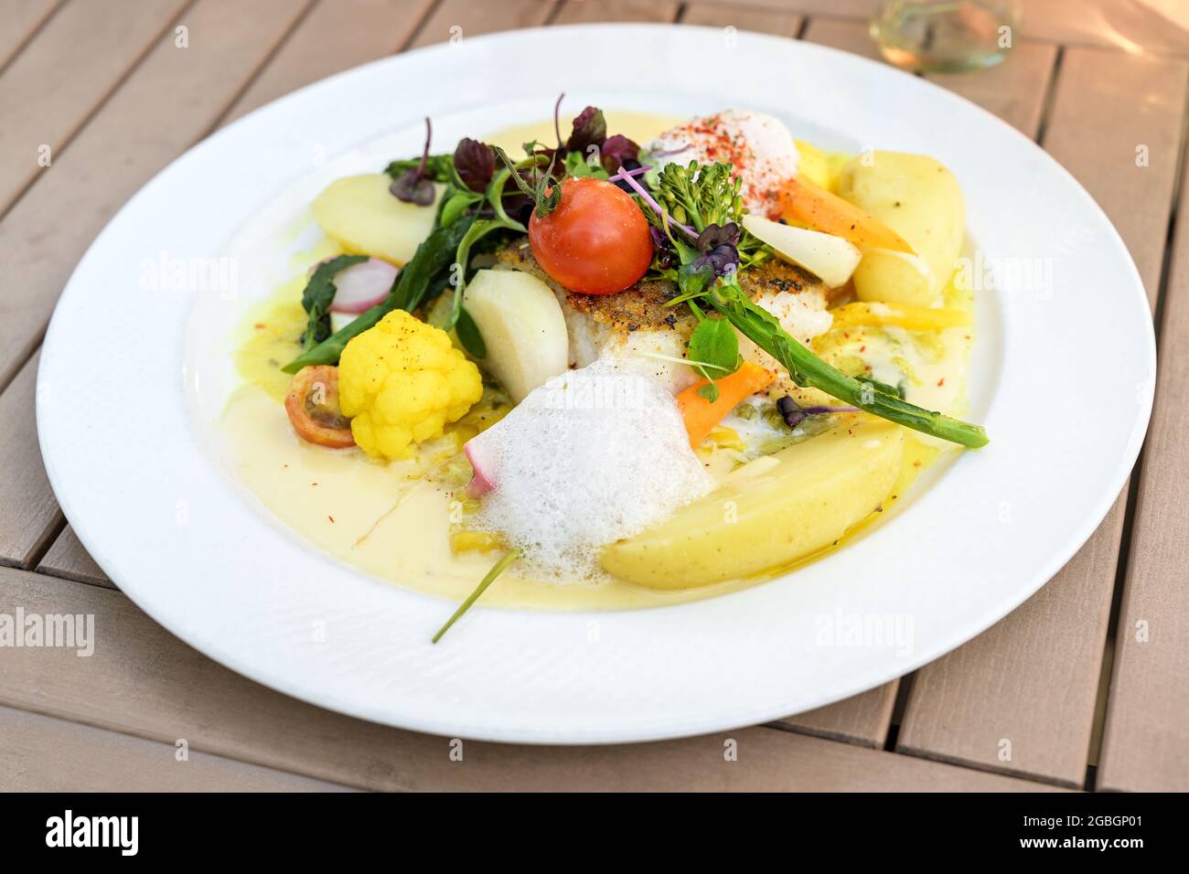 Légumes avec du poisson frit et des pommes de terre en sauce safran, garni d'herbes et de mousse sur une assiette blanche et une table en bois, foyer choisi, étroit de Banque D'Images