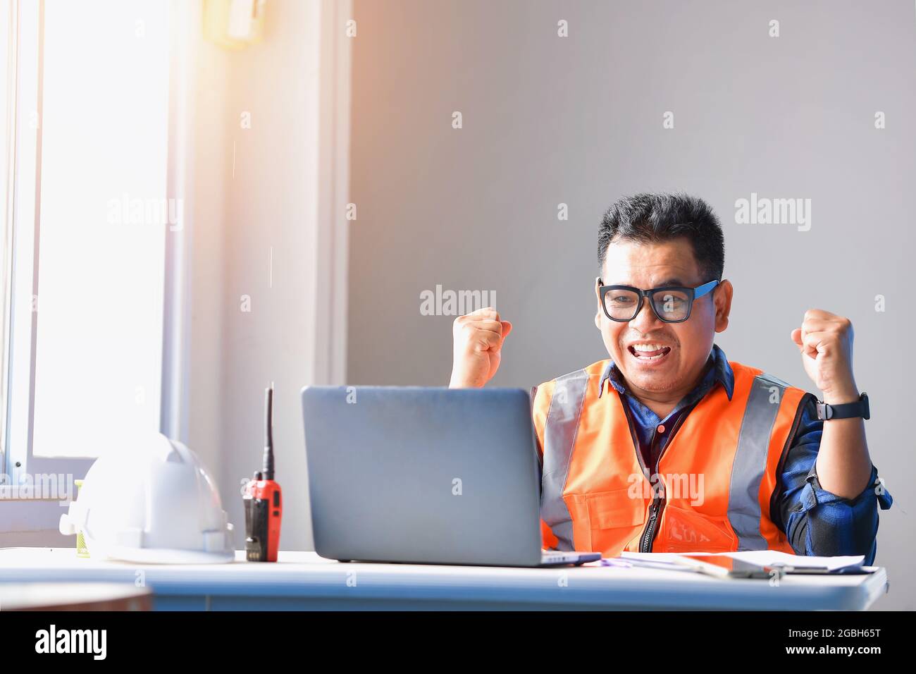 Ingénieur souriant assis à son bureau pour célébrer avec ses mains dans l'air Banque D'Images