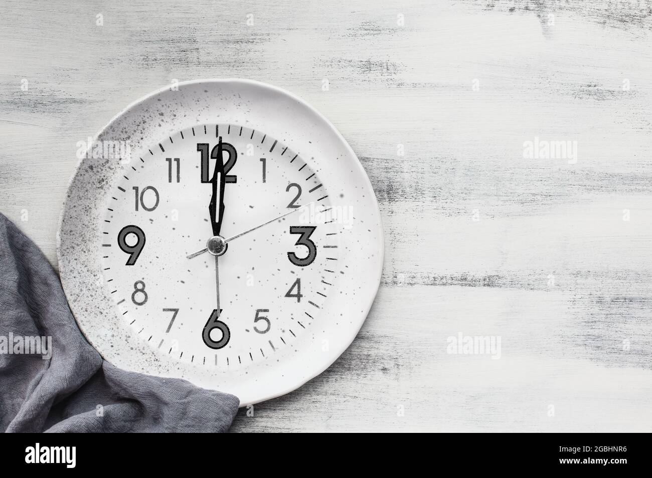 Pose plate d'une horloge blanche à pois avec serviette sur une table en bois rustique avec espace pour copier le concept de jeûne intermittent. Banque D'Images