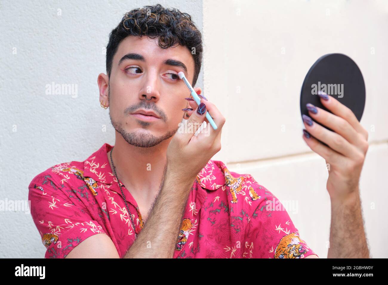 Jeune homme caucasien avec de longs ongles faux appliquant l'ombre des yeux rouges dans la rue. Banque D'Images