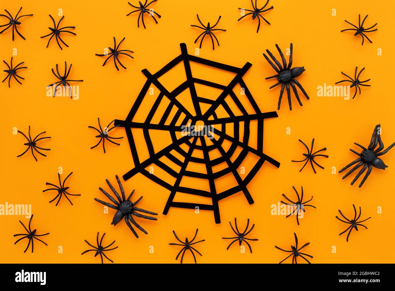 Arrière-plan Halloween avec araignées décoratives et toile d'araignée sur fond orange vif. Vue de dessus Banque D'Images