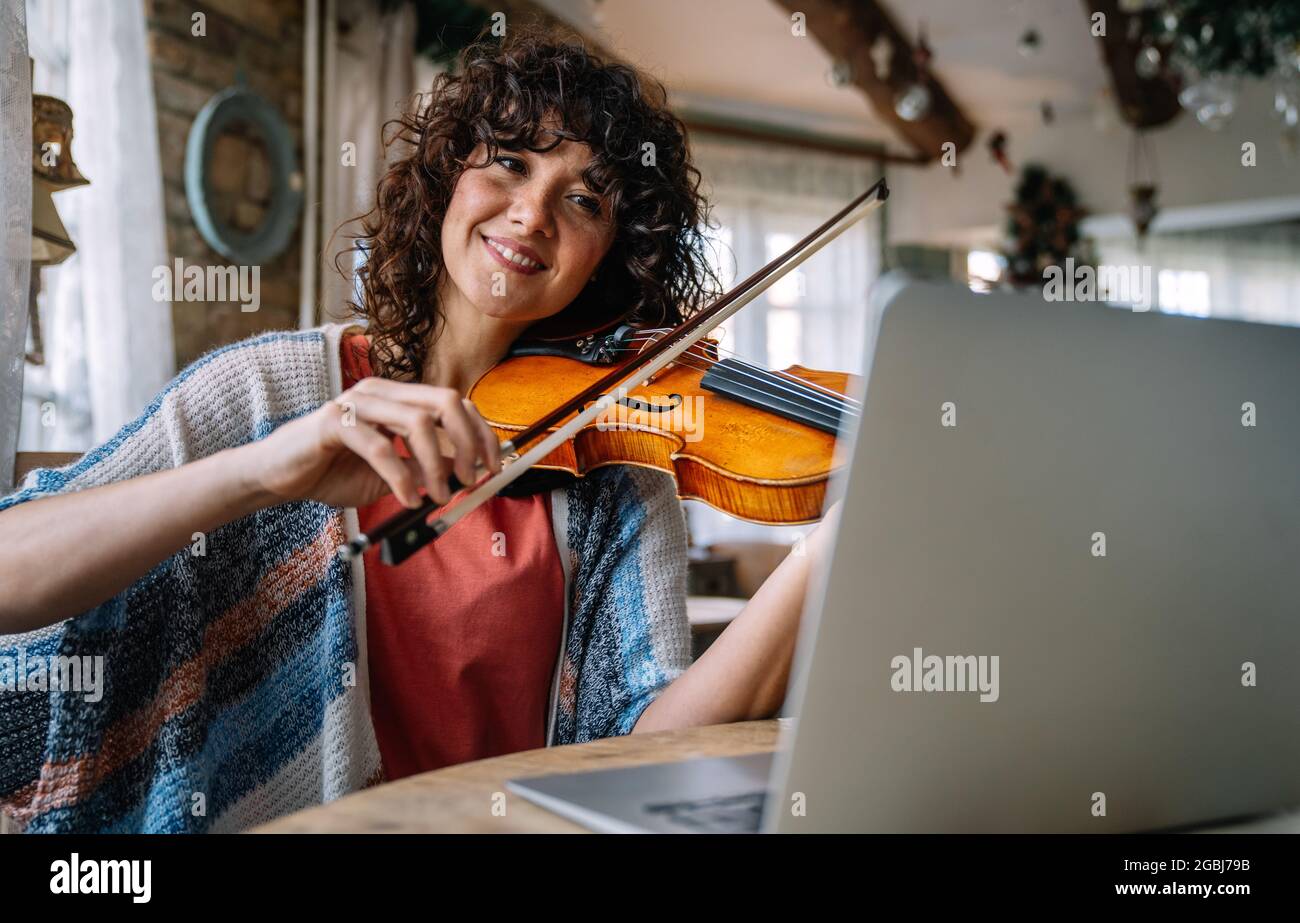 Une étudiante apprend à jouer du violon en ligne à l'aide d'un ordinateur portable. Banque D'Images