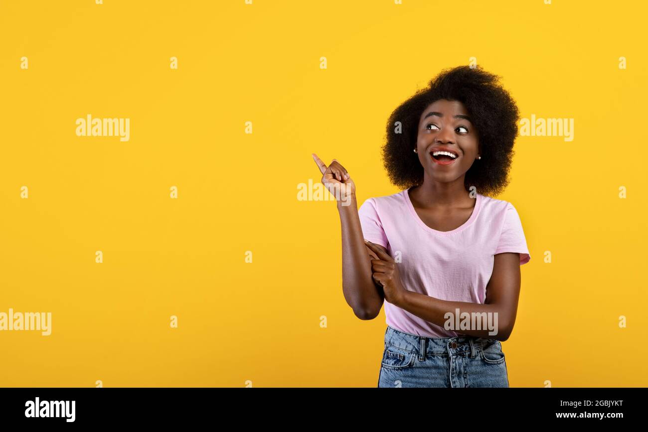 Solde saisonnier. Affective afro-américaine dame pointant sur l'espace vide sur fond jaune studio, conception de bannière Banque D'Images