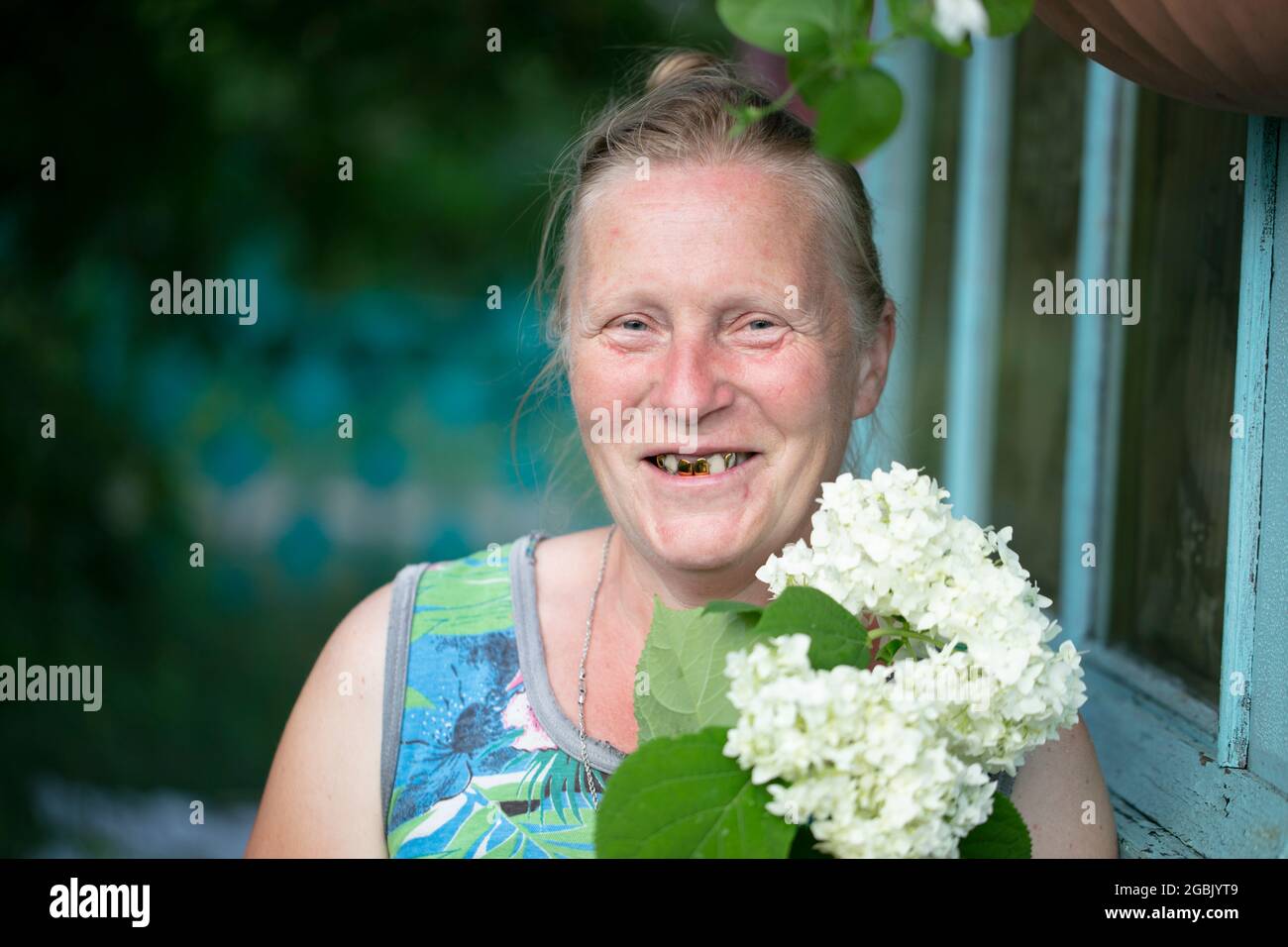 Portrait d'une vieille femme joyeuse aux dents dorées et fleurs blanches. Banque D'Images