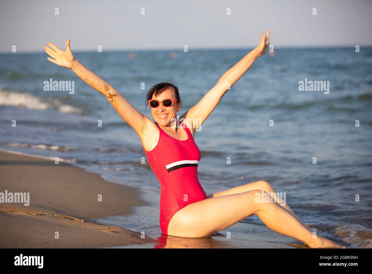 Femme heureuse à la mer dans le soleil. Femme dans un maillot de l'eau éclabousse sur fond de vagues. Vacances d'été sur la plage. Banque D'Images