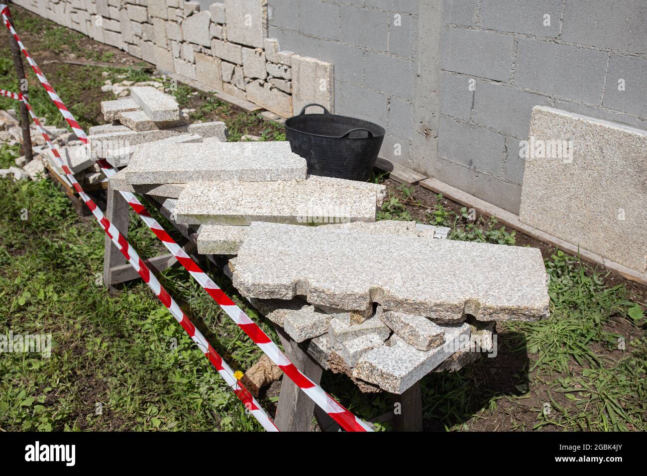 Le mur du bloc de cinder est doublé de dalles de granit en pierre sur le chantier de construction extérieur. Décoration murale Banque D'Images
