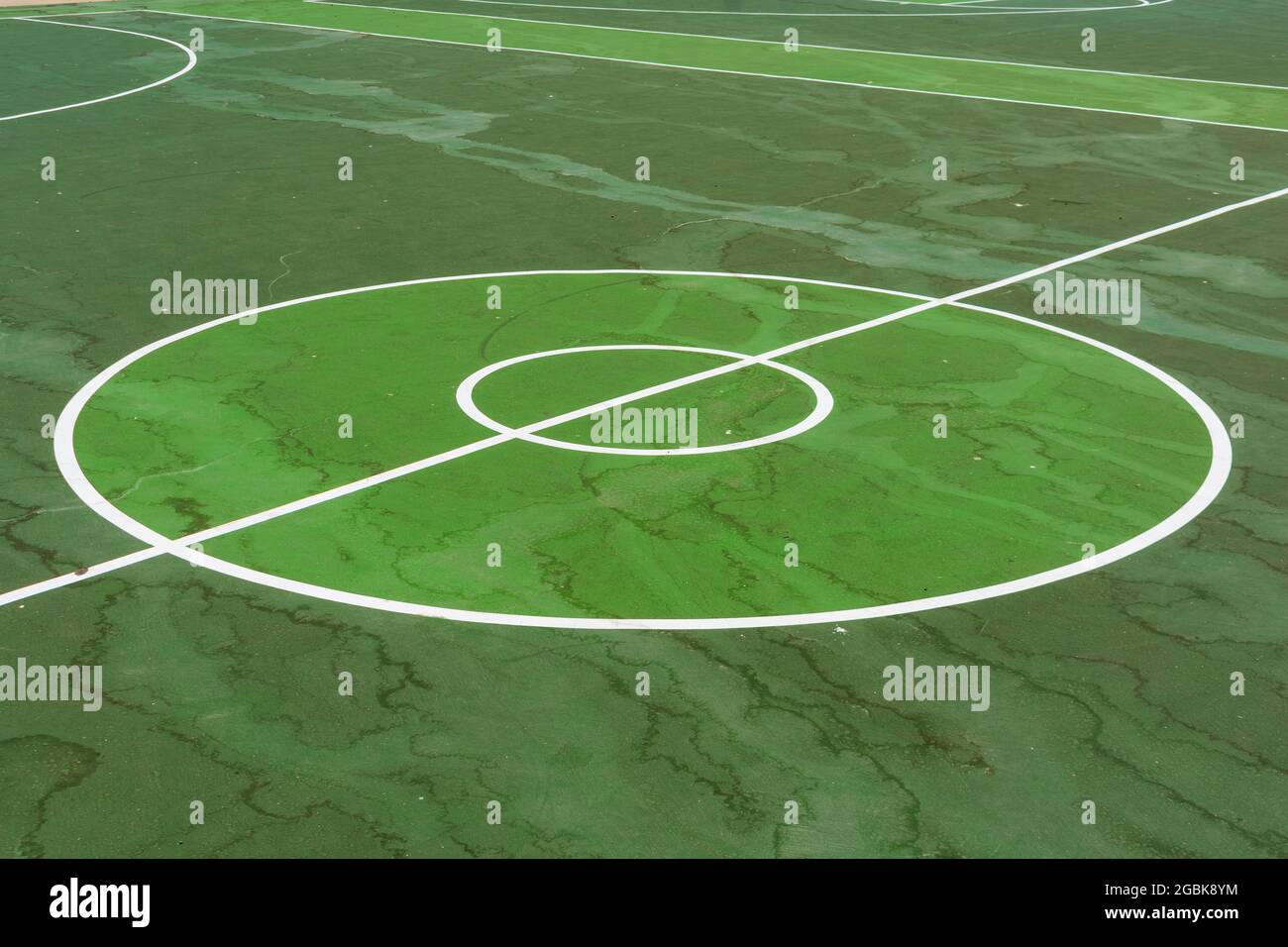Deux cercles de saut au centre et une ligne de division sur un terrain de basket-ball extérieur vert recouvert de taches d'eau. Banque D'Images