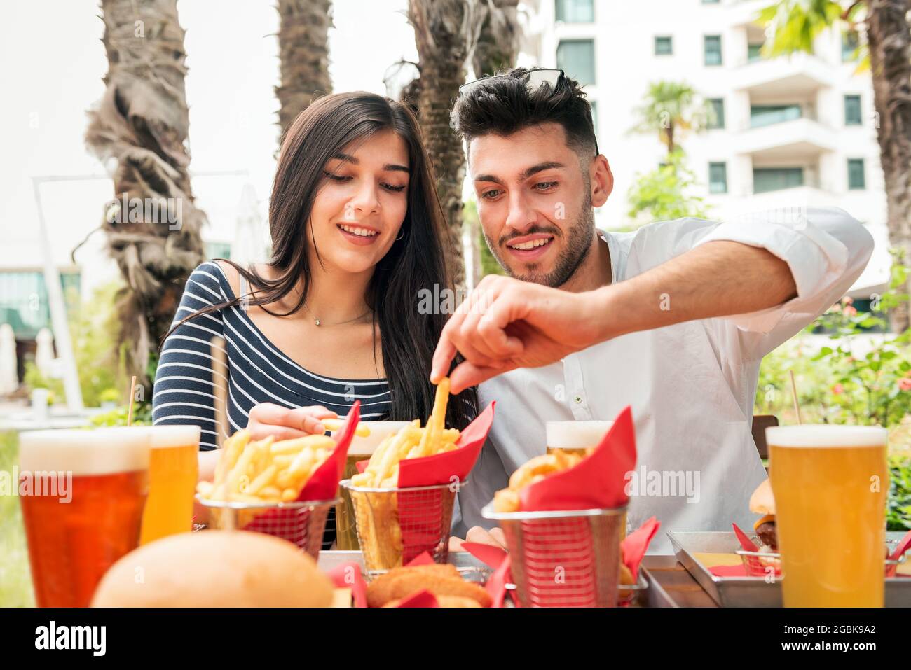 Un jeune couple mange des frites croustillantes ou des chips à une table extérieure dans un restaurant ou un pub dans une ville accompagné de verres de bière froide Banque D'Images