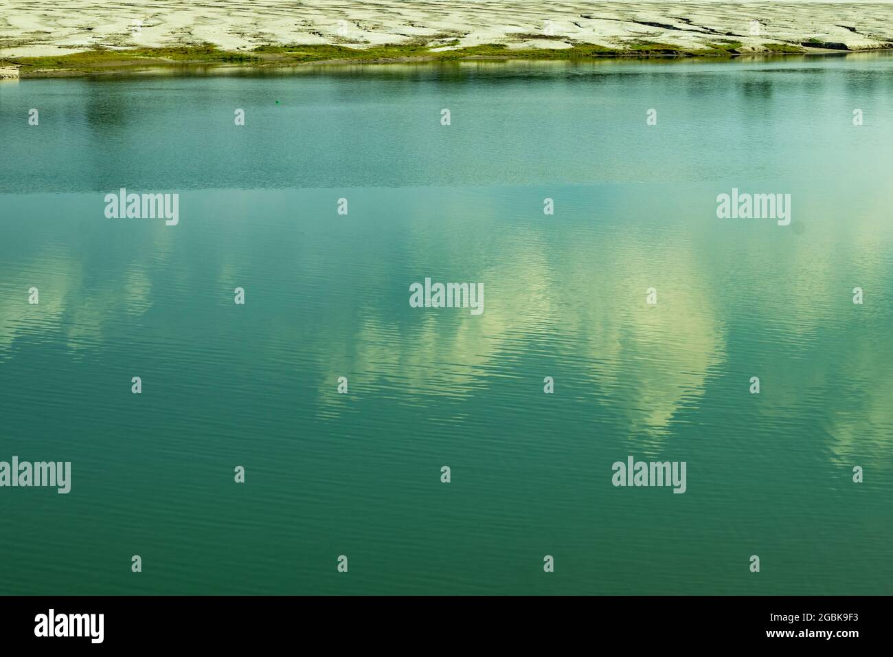 L'eau de la rivière bleue et tant de petites herbes sur la rive et bleu océan faisant une énorme éclaboussure et ombre d'un nuage blanc sur l'eau Banque D'Images