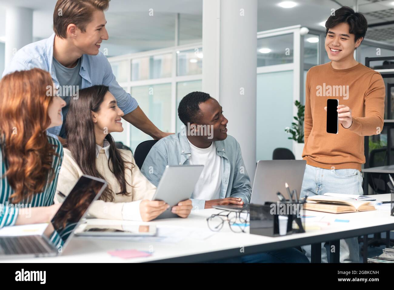 Groupe diversifié d'étudiants assis au bureau, un gars montrant le téléphone Banque D'Images