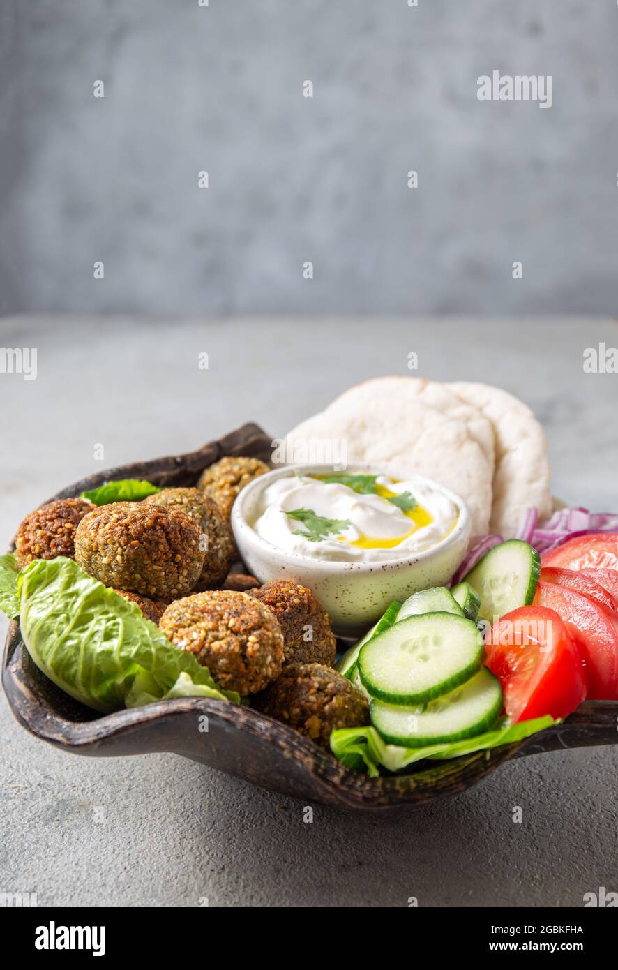 Falafel, légumes frais et pain pita sur plaque d'argile, fond gris Banque D'Images