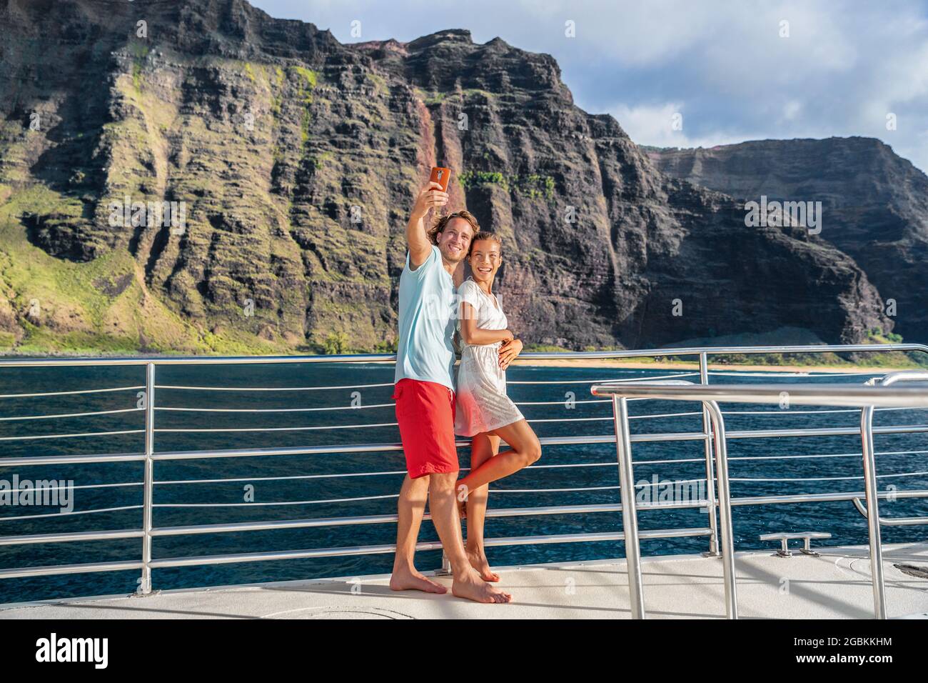 Un bateau de croisière à Hawaï couple de touristes prenant le selfie avec un téléphone portable à la côte de Na Pali célèbre attraction dans l'île de Kauai, paysage majestueux et spectaculaire Banque D'Images