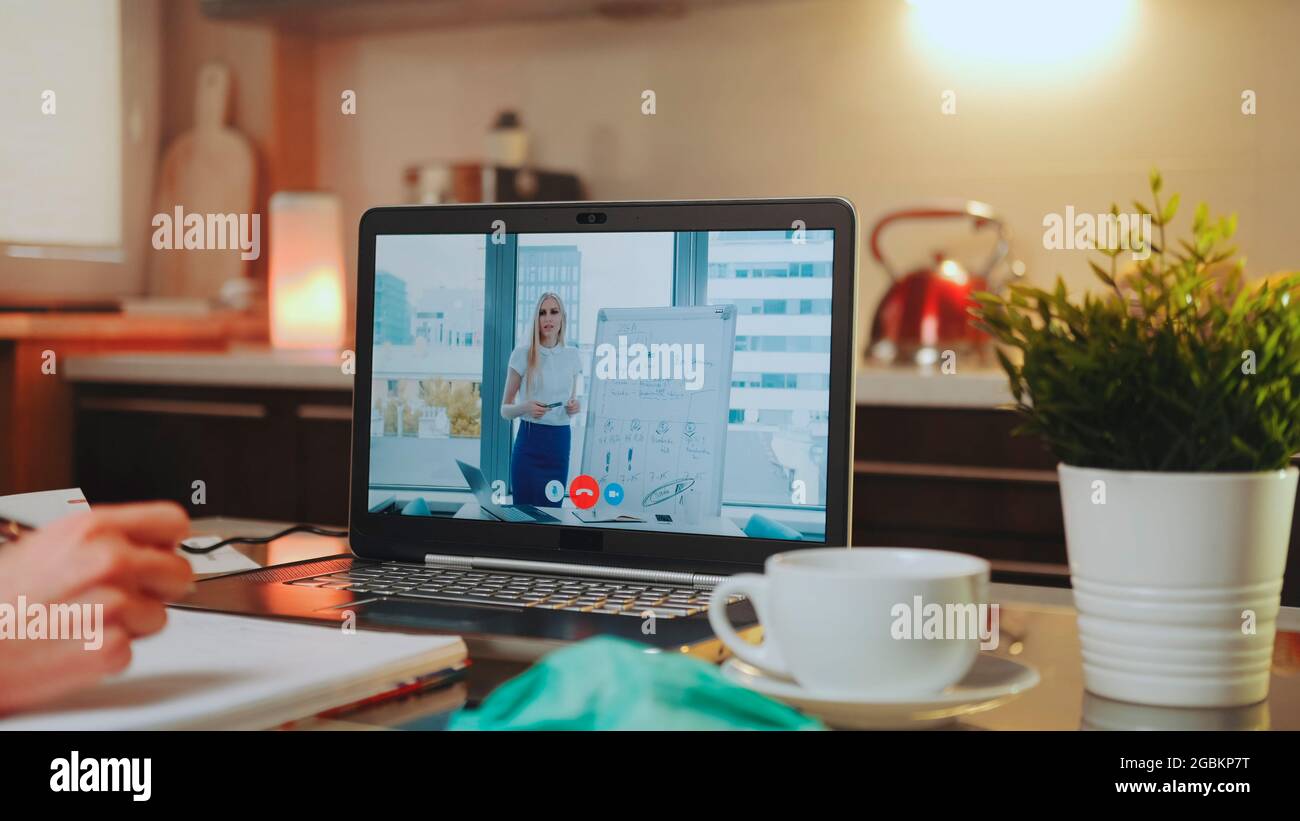 Vidéoconférence en ligne sur ordinateur portable avec enceinte féminine au bureau à domicile. Au premier plan : écriture des mains, masque médical et une tasse. Banque D'Images