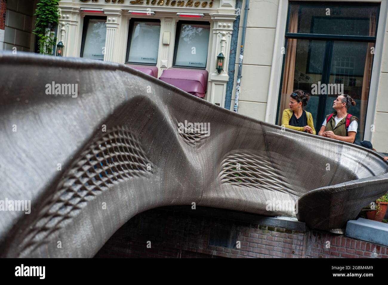 Un couple regarde la fin du pont.UN pont piétonnier de 12 mètres imprimé en 3D conçu par Joris Laarman et construit par la société néerlandaise de robotique MX3D a été ouvert à Amsterdam six ans après le lancement du projet. Le pont, qui a été fabriqué à partir de tiges en acier inoxydable par des bras robotisés à six axes équipés de matériel de soudage, traverse l'Achterburgwal d'Oudezijds, dans le quartier rouge d'Amsterdam. La structure a été renforcée afin d'être plus conforme aux règlements du conseil et de protéger la structure contre tout risque de collision avec un bateau. Banque D'Images