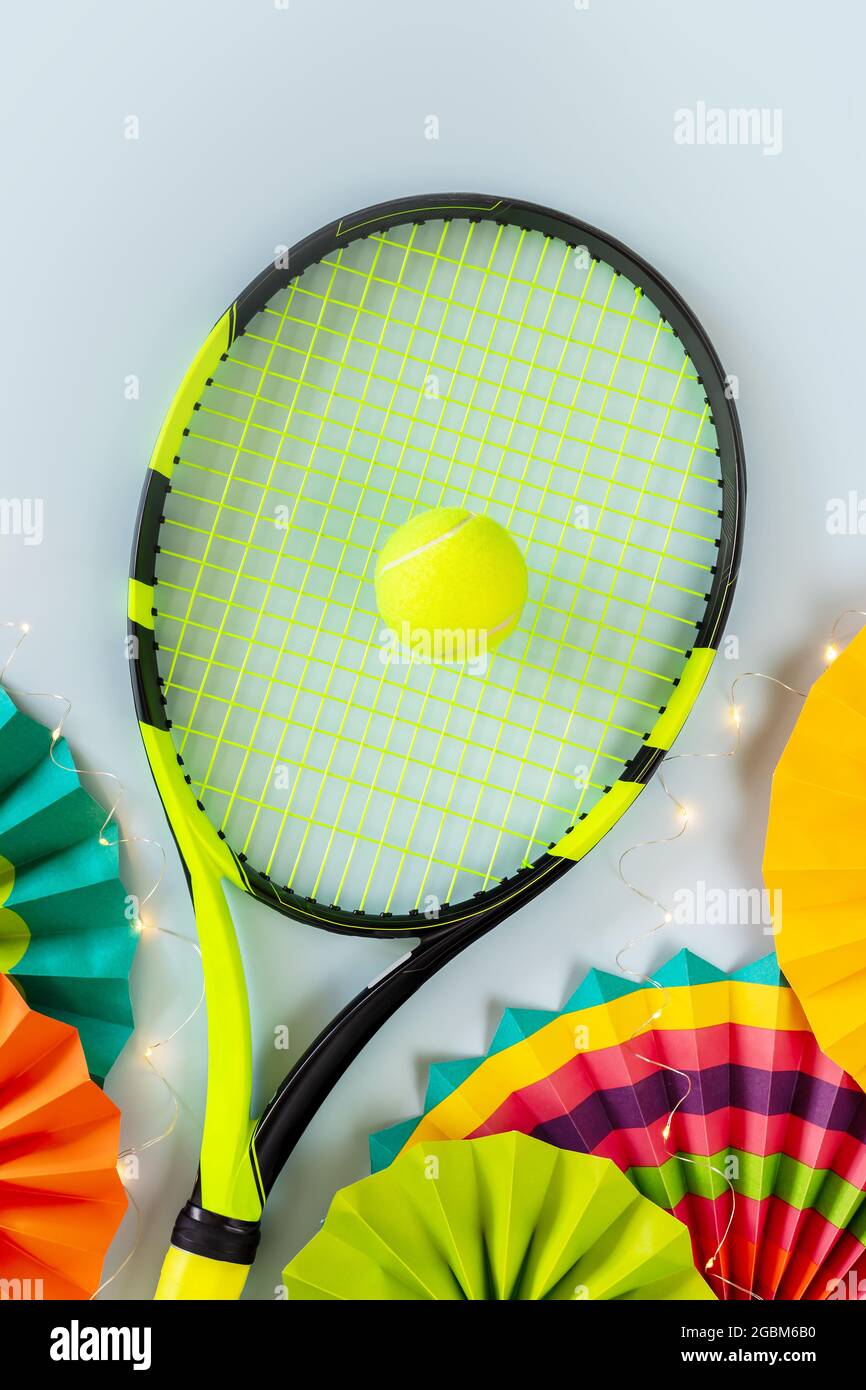 Composition de tennis avec raquette, balle de tennis jaune, fans de papier coloré et guirlande lumineuse sur fond bleu. Bannière des fêtes pour un concours de tennis Banque D'Images