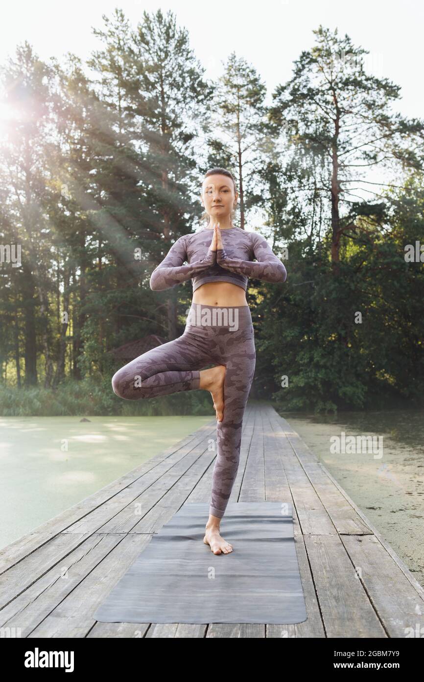 Une femme pratiquant le yoga, le matin sur un pont en bois dans le parc, exécute l'exercice vrikshasana, pose d'arbre Banque D'Images