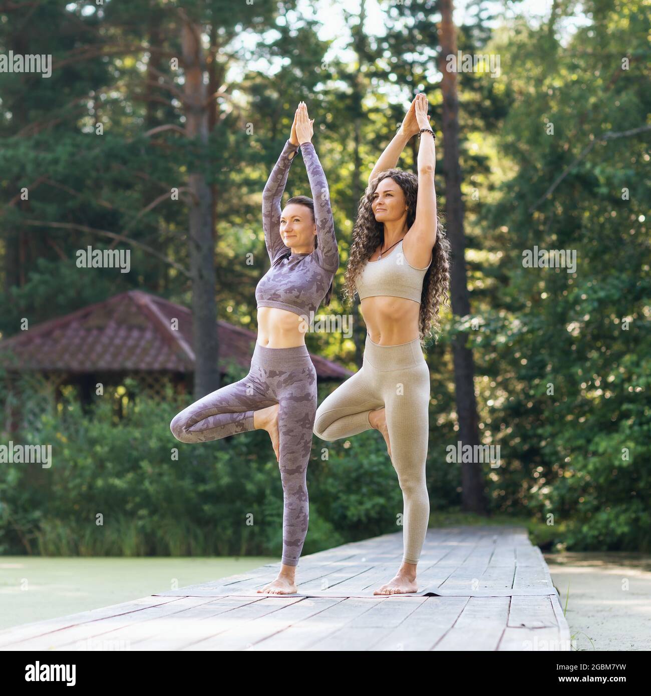 Deux femmes pratiquant le yoga, le matin sur un pont en bois dans le parc, effectuent un exercice vrikshasana, pose d'arbre Banque D'Images