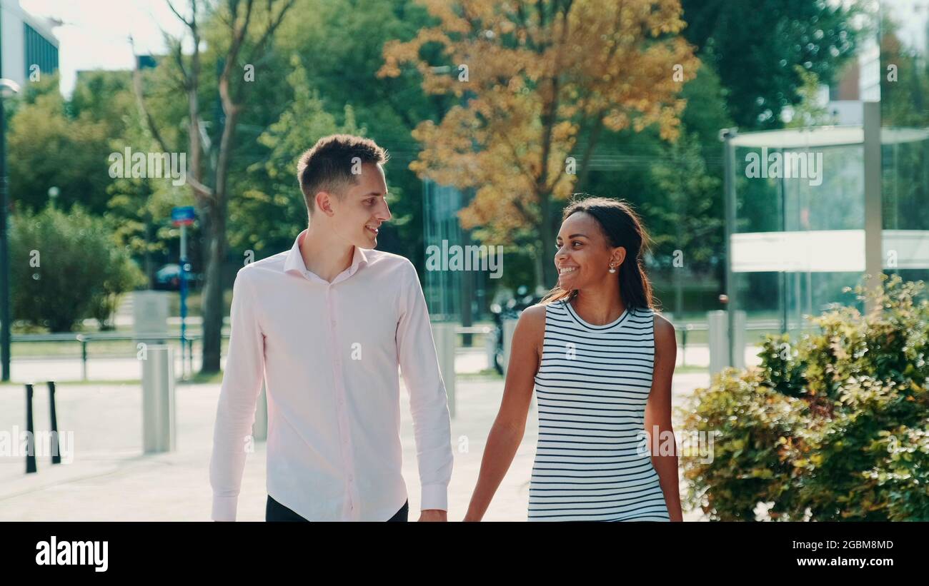 Les couples multiethniques se regardent en se promenant dans la rue, en tenant les mains et en parlant. Concept de relation. Banque D'Images