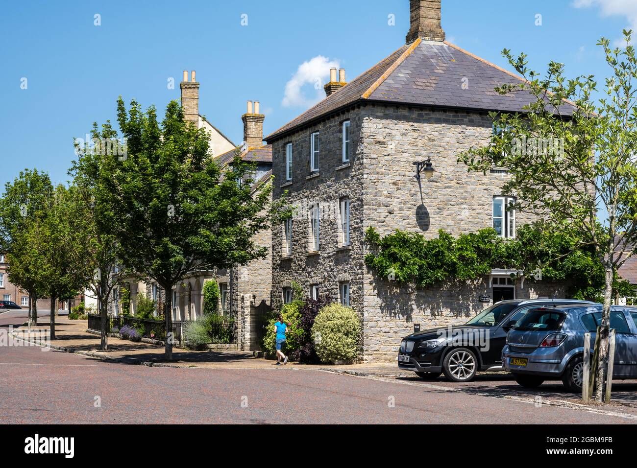 Un jogger passe devant de nouveaux chalets en pierre et des arbres de rue dans la nouvelle ville de Poundbury, Dorset. Banque D'Images