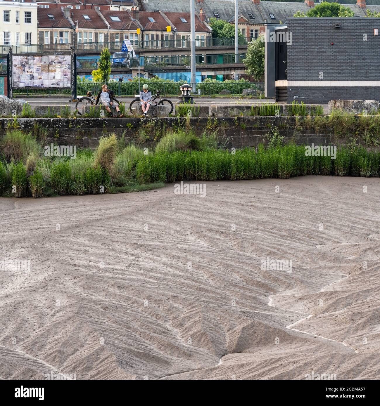 Les cyclistes s'assoient sur un quai près de l'écluse d'entrée du port flottant de Bristol à marée basse sur la rivière Avon. Banque D'Images