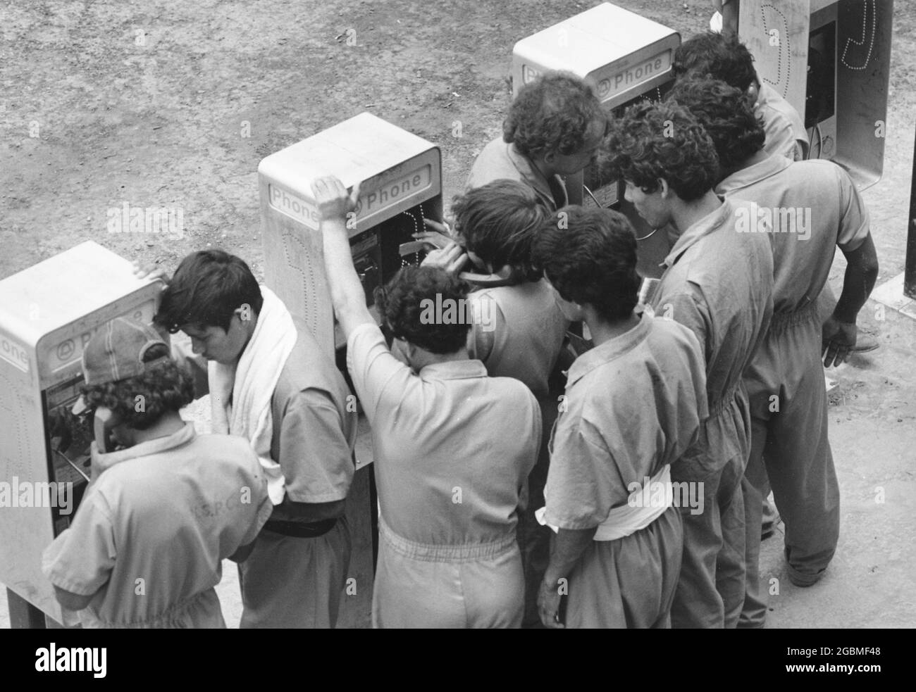 Port Isabel, Texas, États-Unis, circa1989 : les immigrants sans papiers du centre de détention du sud du Texas se réunissent autour de téléphones payants pour appeler des membres de la famille ou un avocat. ©Bob Daemmrich Banque D'Images