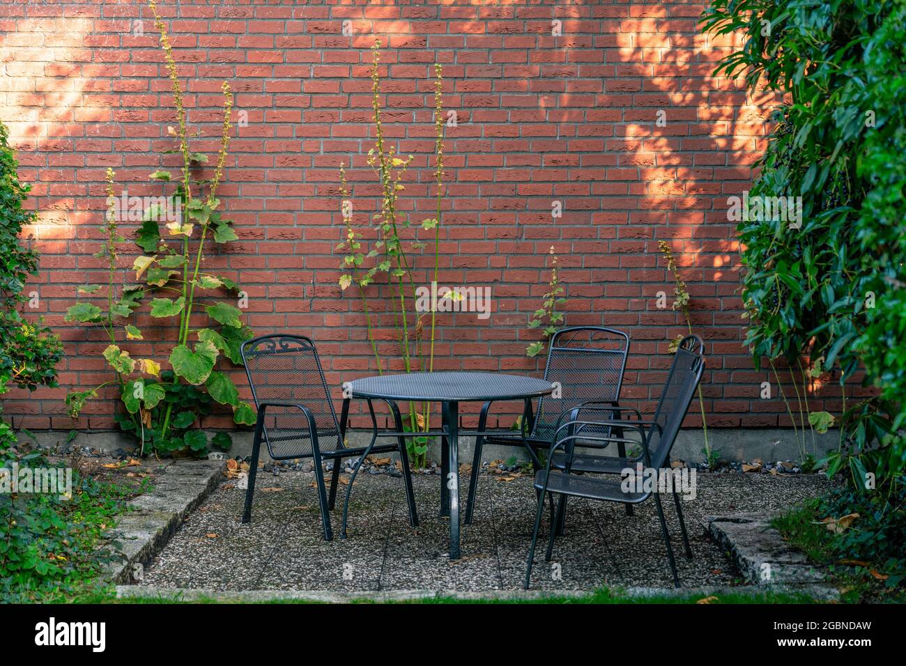 Table en métal noir avec 3 chaises à l'extérieur dans le jardin devant un mur de briques Banque D'Images