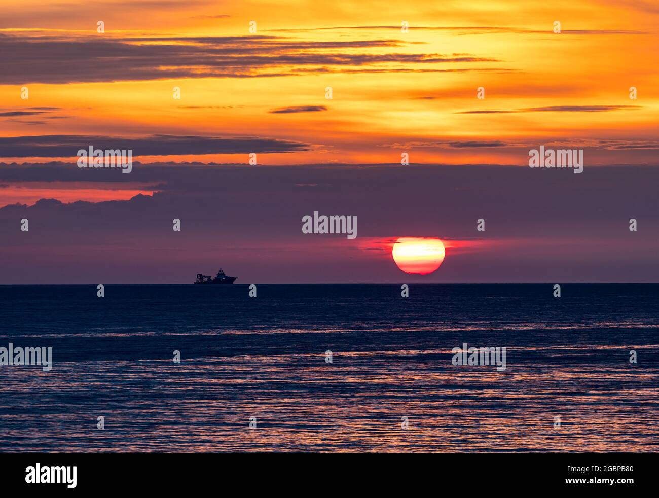 Écosse, Royaume-Uni, 5 août 2021. Lever du soleil : le soleil se lève au-dessus de l'horizon avec la silhouette d'un navire dans la mer du Nord Banque D'Images