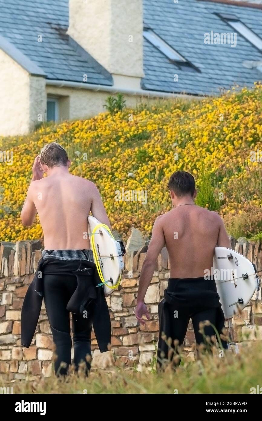 Vue arrière de deux jeunes surfeurs mâles fatigués transportant leurs planches de surf marchant le long du sentier côtier sur la Pointe de Newquay en Cornouailles. Banque D'Images