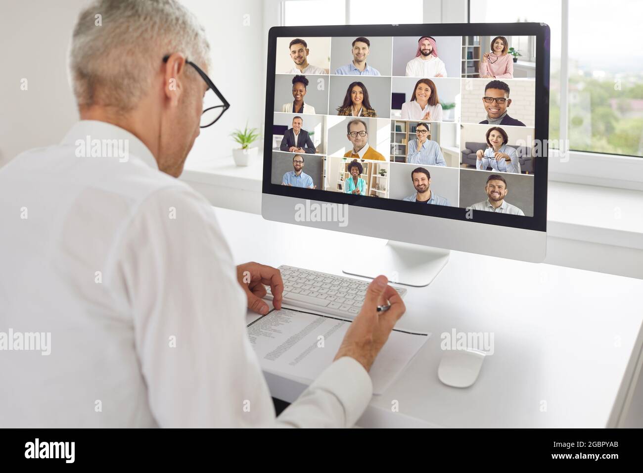 Homme assis à un bureau avec ordinateur et ayant une réunion en ligne avec une équipe d'affaires diversifiée Banque D'Images